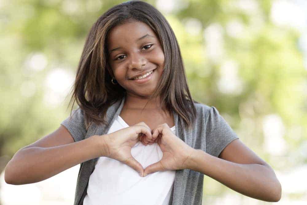 smiling girl uses her hands to form a heart shape