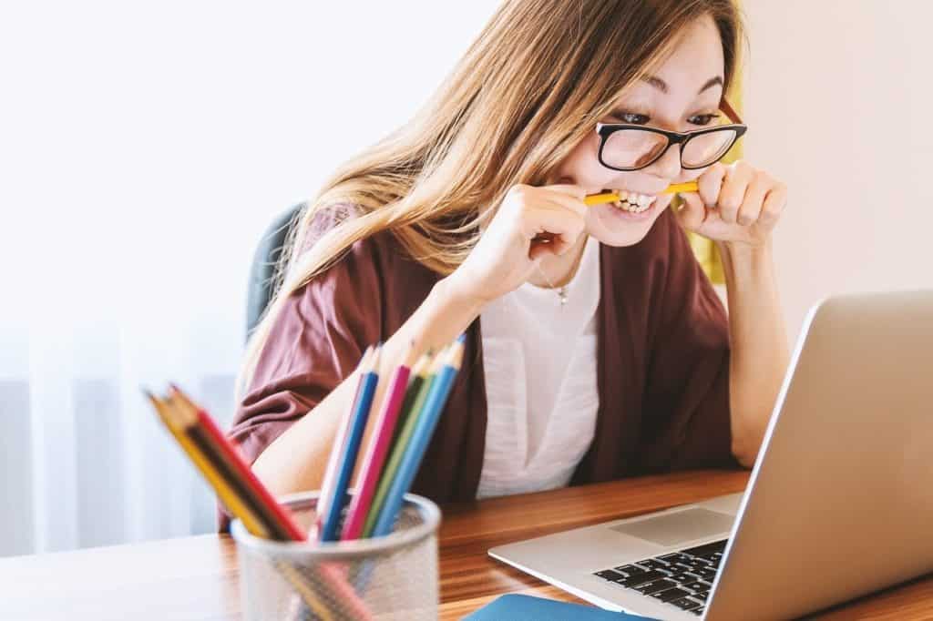 woman biting pencil in frustration as she stares at the laptop on her desk